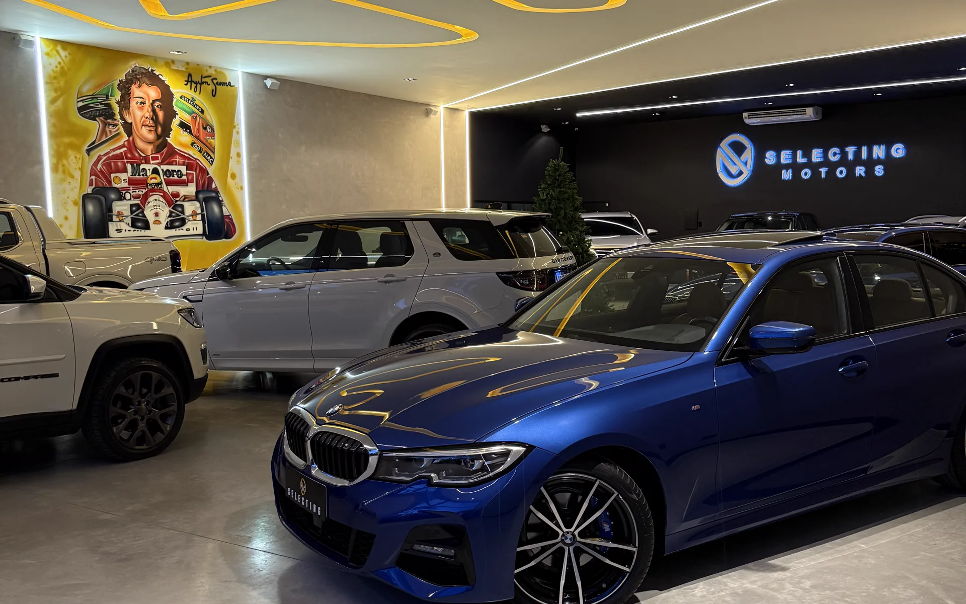 Salão da Selecting Motors: veículos expostos sob a fita de luz dourada, com o letreiro da marca ao fundo